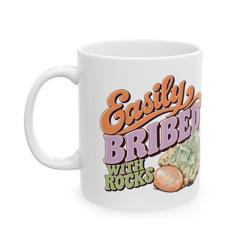 White Easily Bribed with Rocks ceramic mug with retro orange and purple lettering, green crystal artwork and an orange stone — handle-right view.